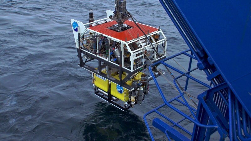 Ein Träger bringt das gelbe ROV ins Challenger-Tief. In 7000 Meter Tiefe gibt er das ROV frei. Nur über ein dünnes Kabel mit dem Träger verbunden, soll das ROV in etwa 11 Kilometer Tiefe agieren. – Bild: ZDF/​NHK