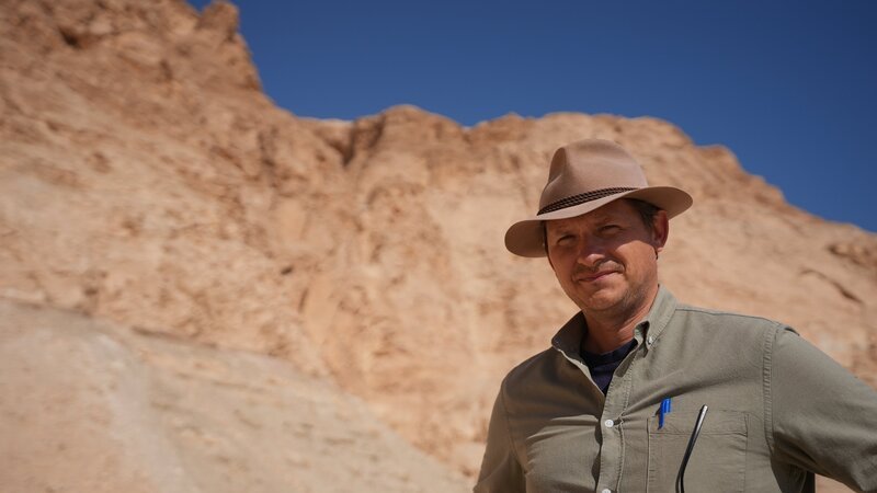 Der Archäologe Patryk Chudzik steht vor den Klippen von Deir el-Bahari. – Bild: Windfall Films/​Andrew Richens