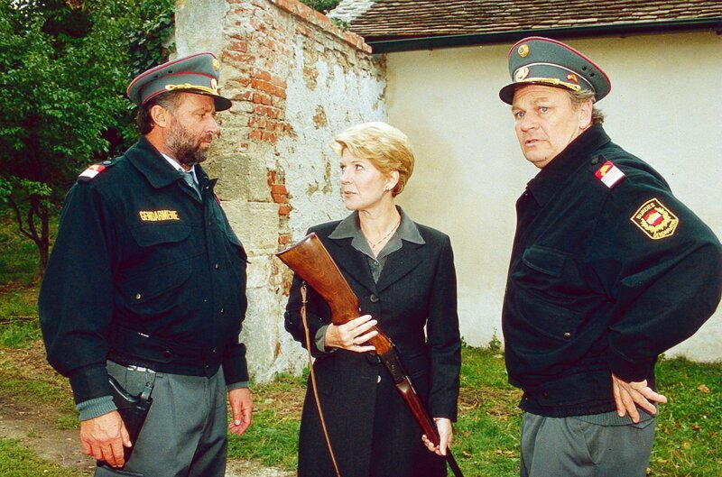 Julia Laubach übergibt die Waffe von Fritz Holzer an die beiden Gendarmen (v.li.: Ludwig Dornauer, Christiane Hörbiger, Michael König). – Bild: ORF III