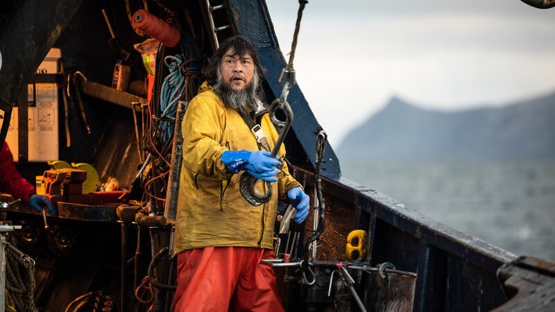 Saga-Deckhelfer Mac hält den Picking-Haken. – Bild: Warner Bros. Discovery