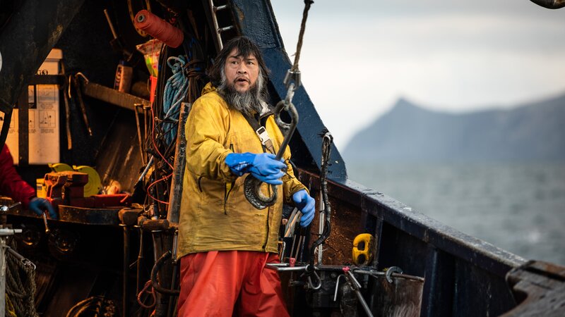 Saga-Deckhelfer Mac hält den Picking-Haken. – Bild: Warner Bros. Discovery