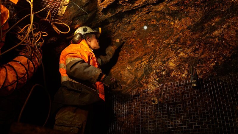 A miner inspecting a rock face underground. – Bild: Prospero Productions
