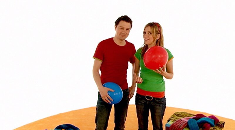 Tanja und André versuchen, sich Jacke, Handschuhe und Schal anzuziehen, während sie einen Ballon in der Luft halten. – Bild: WDR