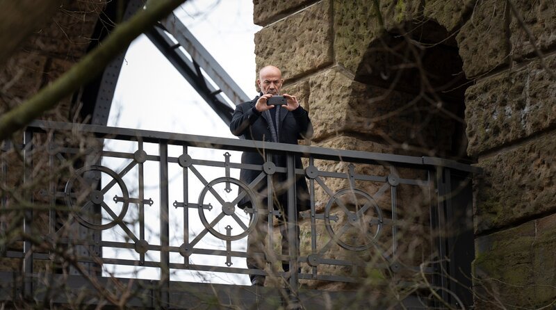 Der ehemalige Kommissar Hagen Benz (Heiner Lauterbach) fotografiert den Tatort aus der Ferne. – Bild: ARD Degeto Film/​filmpool fiction GmbH/​Christine Schroeder
