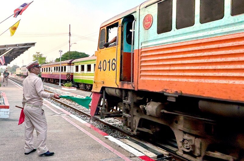 Mit grünen Fahnen geben die Fahrdienstleiter an den thailändischen Bahnhöfen die Einfahrt frei. – Bild: SWR/​Kirsten Ruppel