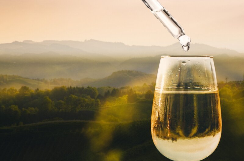Pipette über einem gefüllten Weinglas vor hügeliger Landschaft. Keyvisual „Der große Weinskandal“. – Bild: SWR und stock.adobe.com