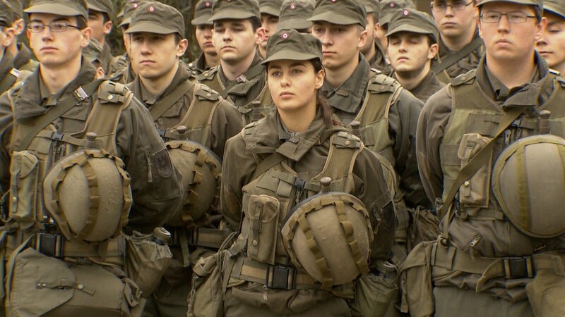 Soldatin umgeben von Wehrmännern. – Bild: ORF