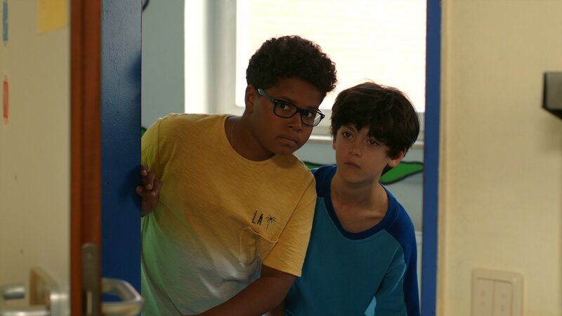 Kofi (Mathieu Noël) und Piet (Noah Lusander) lauschen an Arnes Bürotür. – Bild: NDR/​Letterbox