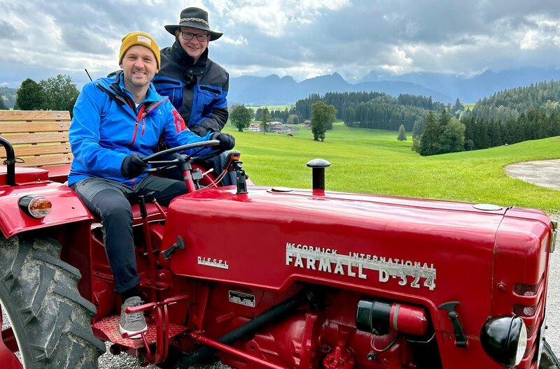 Das Allgäu: Moderator Johannes Zenglein (l.) mit dem Traktor auf entschleunigter Reise unterwegs zwischen hohen Bergen und wunderschönen Seen. (r.: Traktor-Verleiher Michael Strobel) – Bild: SWR