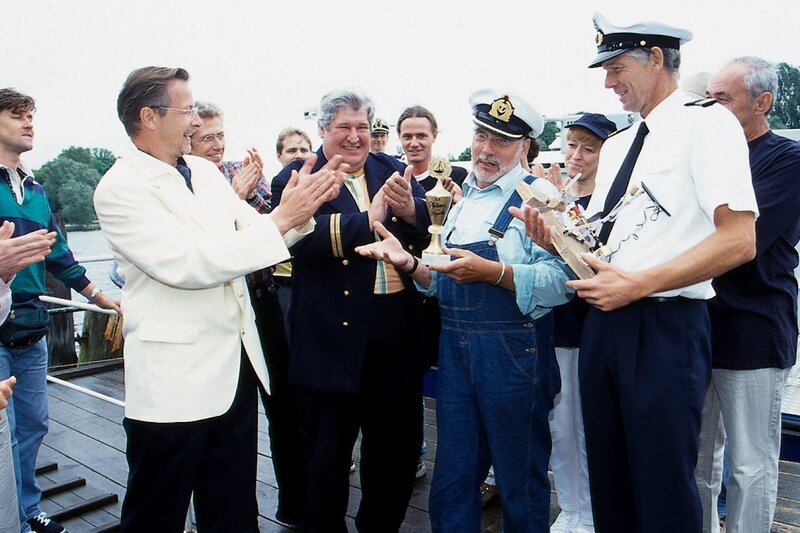 Peter (Peter Lustig, 2.v.r.) erhält für sein solarbetriebenes Boot den ersten Preis der Bärstädter Pfützenregatta. – Bild: ZDF