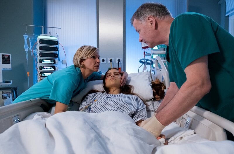 Bea Hölsch (Daniela Wutte, re.) ist mit Fieber umgekippt und hat sich einen Schlüsselbeinbruch zugezogen. Ihren behandelnden Arzt Dr. Martin Stein (Bernhard Bettermann, li.) bringt sie mit ihrem sehr anschmachtenden Verhalten in eine ziemlich unangenehme Situation. Auch Dr. Kathrin Globisch (Andrea Kathrin Loewig, mi.) ist ziemlich irritiert. – Bild: MDR/​Saxonia Media/​Sebastian Kiss