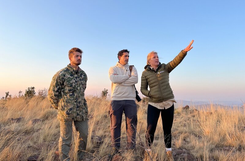 Marios Michaelidis (M.) und Lea Henzgen (r.) von der AMES-Foundation mit Security-Chief Tyler Michael (l.) auf dem Sonop-Berg. Sie blicken auf das Dabchick Wildlife Reservat sowie angrenzende Ländereien. Ihr Plan: Durch Biodiversity Credits wollen sie Geld einnehmen, um das Reservat zu vergrößern. – Bild: phoenix/​ZDF/​Jochen Klöck