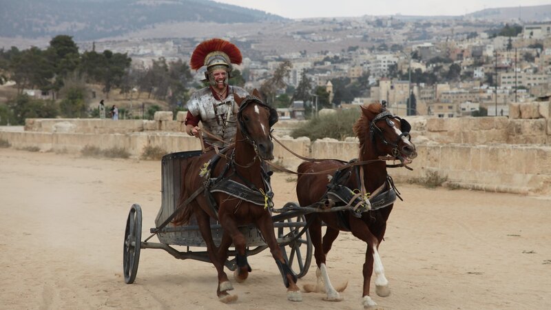 Josh Gates fährt als römischer Zenturio verkleidet auf einem Streitwagen in Amman, Jordanien. – Bild: Discovery Communications