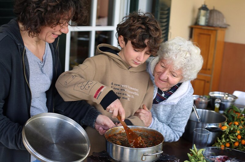 Alexandra Guliumis (li.) experimentiert mit frisch geernteten Kumquats. Ihr Sohn Stelis (Mi.) kocht Tsigareli, ein traditionelles Gericht mit gedünsteten Wildkräutern und Blattgemüse. – Bild: Reiner Bauer