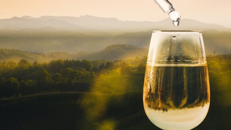 Pipette über einem gefüllten Weinglas vor hügeliger Landschaft. Keyvisual „Der große Weinskandal“. – Bild: ZDF und SWR/​stock.adobe.com