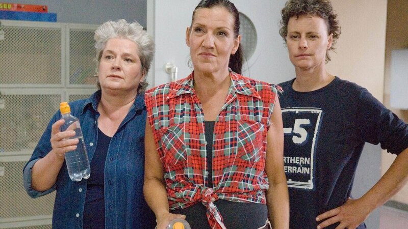 Walter (Katy Karrenbauer) mischt Katjas Glücksspielsrunde auf, indem sie Ilses Schnaps verteilt (mit Uschi und Mel). – Bild: TVNOW /​ Stefan Erhard
