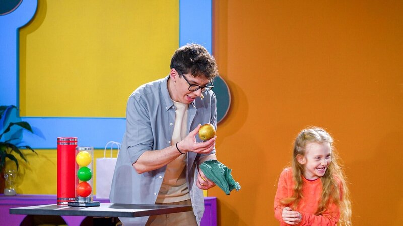 Leonore, ein Kind aus dem Publikum, hilft Christoph Hirschler bei einem lustigen Zaubertrick und zaubert einen Apfel her. – Bild: ORF/​Tambalina Entertainment