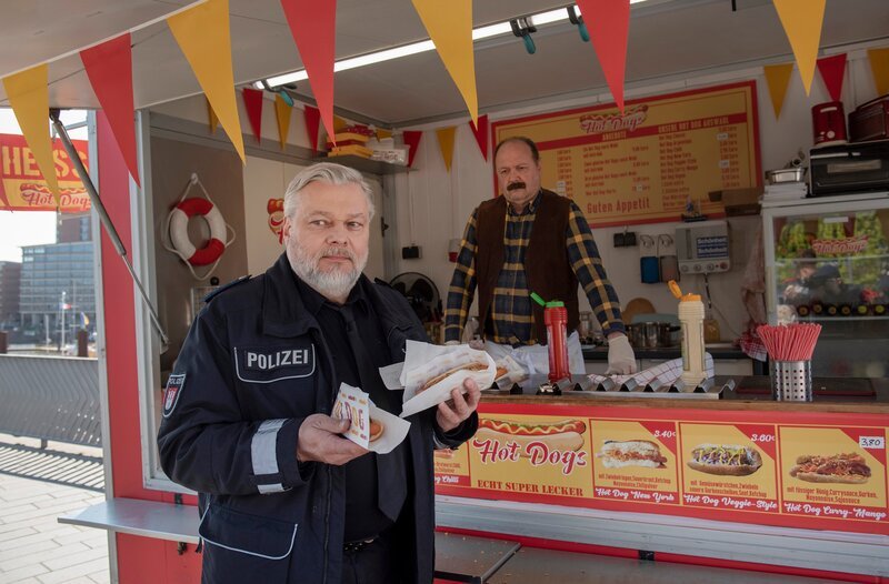 Am Hot-Dog-Stand: Helmut Husmann (Torsten Münchow, l.) ahnt schon, dass da etwas auf ihn zukommt (mit Komparse). – Bild: ARD/​Thorsten Jander