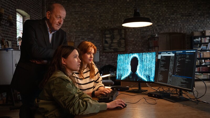 Privatdetektiv Georg Wilsberg (Leonard Lansink, l.) wird von der Studentin Jana Haumann (Lilly Charlotte Dreesen, r.) aufgesucht. Sie will auf einer Tonaufnahme eines digitalen Sprachassistenten eine höchst brisante Ankündigung gehört haben. Undercover begibt Wilsberg sich daraufhin in das Traditionsunternehmen, in dem die Kinder des Eigentümers die Unternehmensnachfolge antreten sollen. Auch Merle (Janina Fautz, M.) hilft mit ihrem technischen Geschick, dem Rätsel auf die Spur zu kommen. – Bild: Thomas Kost /​ ZDF