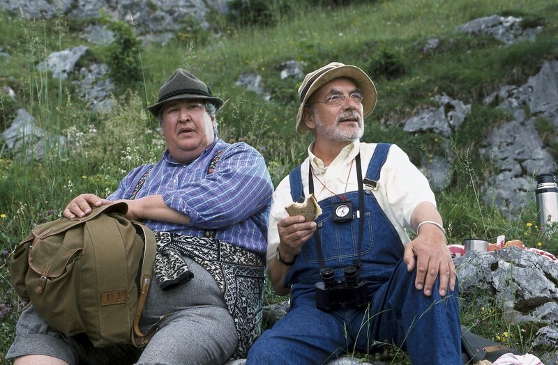Endlich eine Rast bei der Wanderung zur Bergspitze in den Alpen. Herr Paschulke (Helmut Krauss) denkt gleich ans Essen, aber Peter (Peter Lustig) macht Paschulke (Helmut Krauss) auf die wunderbare Pflanzen- und Tierwelt aufmerksam. – Bild: ZDF und Christiane Pausch