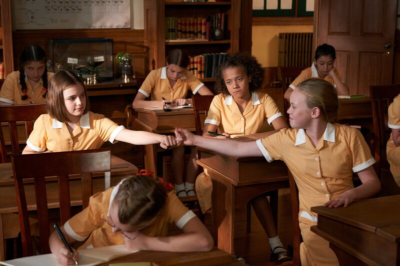 Darrell Rivers (Ella Bright, l.) reicht ihrer neuen Klassenkameradin Gwendoline (Danya Griver, r.) zögerlich ihre Hand zum Freundschaftsgruß. Darrell ist sich unsicher darüber, ob sie mit ihrer launischen Mitschülerin wirklich befreundet sein möchte. Auch Sally (Sienna Arif-Knights, M.) betrachtet die Aktion mit Skepsis. – Bild: ZDF/​DHX – Malory Productions Inc./​Queen Bert Productions