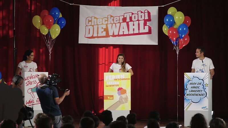 Tobi veranstaltet eine eigene Checker-Wahl. Dafür hat der sich drei Reporter-Kollegen eingeladen: Willi von „Willi wills Wissen“ (re.), Jess von „KI.KA LIVE“ (li.) und Anna von „Anna und die wilden Tiere“ (Mi.). – Bild: BR/​megaherz gmbh/​Hans-Florian Hopfner