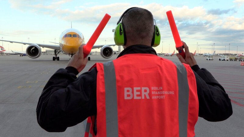 „Auf diesen Moment kommt es an, jetzt darf nichts schief gehen!“ Das neue Dokutainment-Format des rbb, 100% Berlin, bringt uns ganz nah heran an die kleinen und großen Dramen Berlins. Ob auf einer Neugeborenenstation, unterwegs mit dem Zoll oder hinter den Kulissen des BER: Wir erleben hautnah mit, wie viele Menschen Tag und Nacht Großes leisten, um die Stadt am Laufen zu halten. – Timo Krieg winkt eine Boeing 787 ein. – Bild: rbb/​Andreas Graf