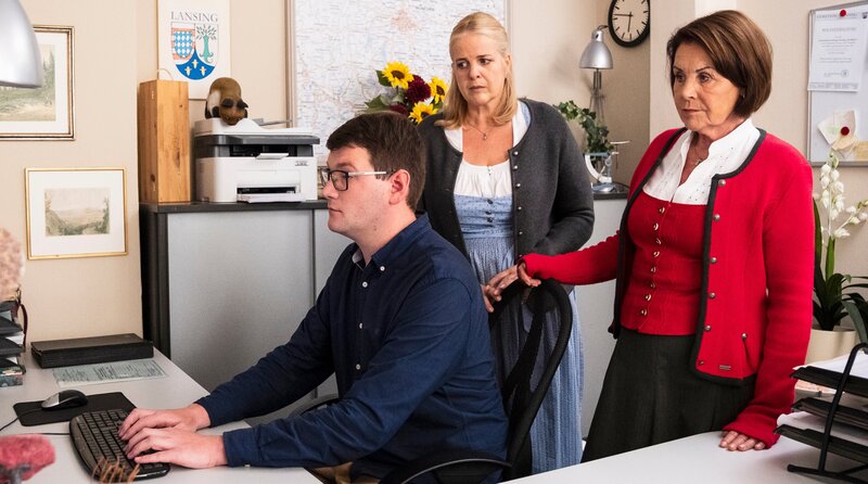 Der IT-Techniker versucht das Computer-Problem in der Amtsstube zu beheben. Von links: IT-Techniker (Paul Steindl), Ulla (Sabrina Dietel, KLD), Rosi (Brigitte Walbrun). Weiteres Bildmaterial finden Sie unter www.br-foto.de. – Bild: BR/​Lena Semmelroggen