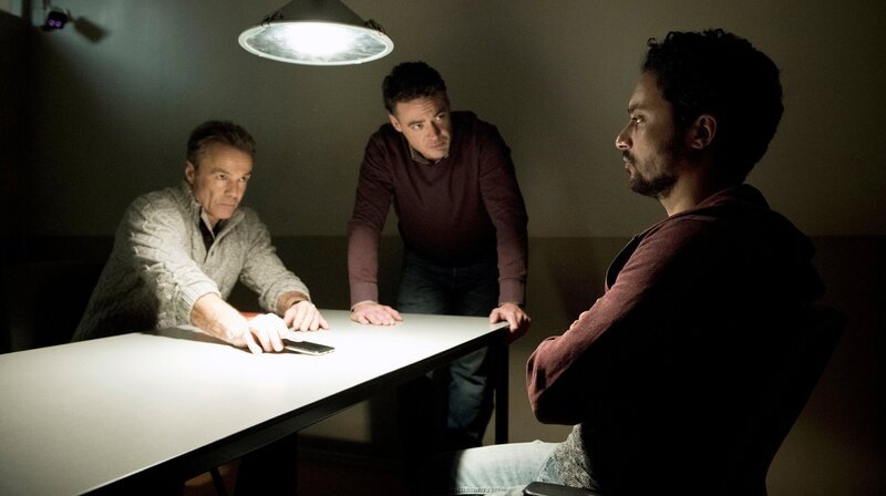 Der einzige Überlebende: LKA-Ermittler Alex Pollack (Hannes Jaenicke, li.) und Kommissar Bram de Groot (Fedja van Huêt) wollen das Schweigen von Molo (Omar El-Saeidi, re.) brechen. – Bild: ARD Degeto/​Martin Valentin Menke