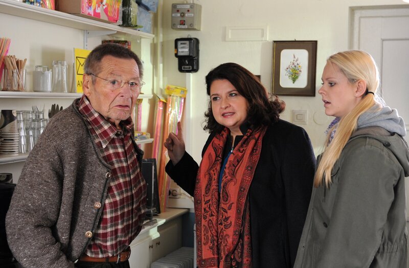 Moni spioniert im Kiosk, um herauszufinden, was der Grund für den geringen Stromverbrauch ist. Von links: Alois Preissinger (Erich Hallhuber), Monika Vogl (Christine Reimer) und Yvonne Preissinger (Alexa Eilers). – Bild: BR/​Marco Orlando Pichler