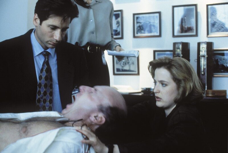 Besessen von einem außerirdischen Wesen, versuchen Mulder (David Duchovny, l.) und Scully (Gillian Anderson, r.), den Projektleiter Colonel Belt (Ed Lauter, vorne) zu befreien. – Bild: TM + Twentieth Century Fox Film Corporation. All Rights Reserved. Lizenzbild frei