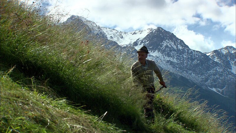 Ein Mann mäht das Gras auf altmodische Weise mit einer Sense. – Bild: ORF III Ein Mann mäht das Gras auf altmodische Weise mit einer Sense. – Bild: ORF III