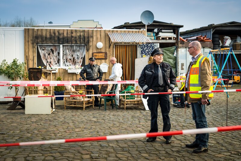 Bei den Berghoffs wurde ein Wohncontainer für Asylbewerber in Brand gesteckt. Tarik (Serhat Cokgezen, l.) und Claudia (Janette Rauch, 2.v.r.) sind vor Ort und lassen sich von den Kollegen der Spurensicherung (Komparsen) eine erste Einschätzung geben. – Bild: ZDF/​Boris Laewen