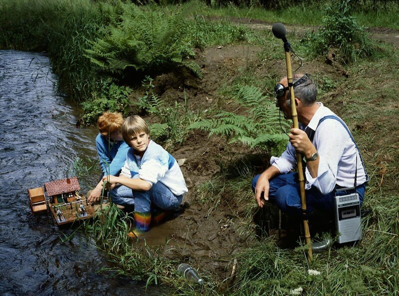 Peter Lustig fragt die beiden Jungs, ob man an dieser Stelle gut das Plätschern des Baches aufzeichnen kann. Er ist auf der Suche nach einer geeigneten Stelle für seine Bach-Komposition. – Bild: ZDF