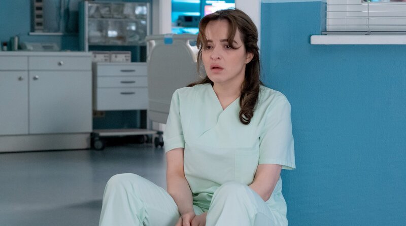 Bea Hölsch (Daniela Wutte, re.) ist mit Fieber umgekippt und hat sich einen Schlüsselbeinbruch zugezogen. Ihren behandelnden Arzt Dr. Martin Stein (Bernhard Bettermann, li.) bringt sie mit ihrem sehr anschmachtenden Verhalten in eine ziemlich unangenehme Situation. Auch Dr. Kathrin Globisch (Andrea Kathrin Loewig, mi.) ist ziemlich irritiert. – Bild: MDR/​Saxonia Media/​Sebastian Kiss