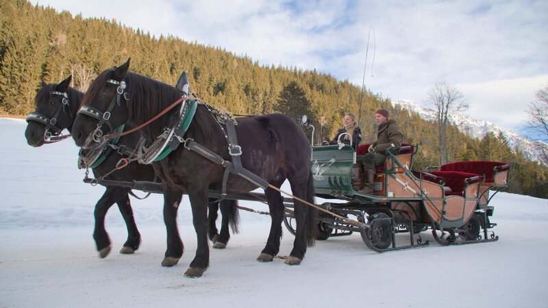 Paula Bründl wird von Landwirt & Pferdezüchter Philipp Pitzer mit dem Pferdeschlitten zur Halseralm gebracht während der Dreharbeiten am 27.01.2025 für ServusTV „Paula kocht – Draußen im Winter“ – Bild: Eckert Film /​ ServusTV /​ Thomas Beckmann
