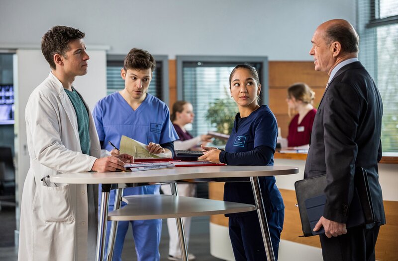 Wolfgang Berger (Horst Günter Marx, r.) kommt zu Dr. Ben Ahlbeck (Philipp Danne, l.), da er sich Hilfe bei der dokumentarischen Arbeit, von den Assistenzärzten erhofft. Werden sich Florian (Lion Wasczyk, 2.v.l.) oder Sofia (Olivia Papoli-Barawati, r.) etwa freiwillig dafür bereit erklären? – Bild: ARD/​Michael Kremer/​Saxonia Media