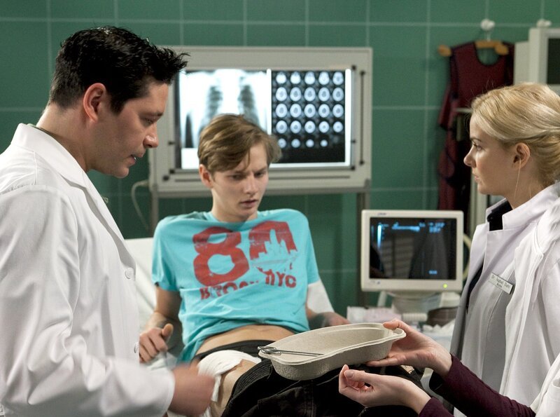 Als Dr. Philipp Brentano (Thomas Koch, links) die Schürfwunde von Rufus Fehn (Joseph K. Bundschuh) untersucht, entdeckt er, dass sich ein gefährlicher Gasbrand entwickelt hat. Brenatano macht Dr. Isabel Dahl (Denise Zich, rechts) Vorwürfe, Rufus nicht eingehend genug untersucht zu haben. – Bild: MDR/​Krajewsky