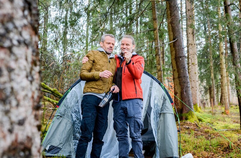 Erik (Sven Waasner, l.) und Michael (Erich Altenkopf, r.) feiern sich stolz als Überlebende einer Bärenattacke. – Bild: ORF/​ARD/​Christof Arnold