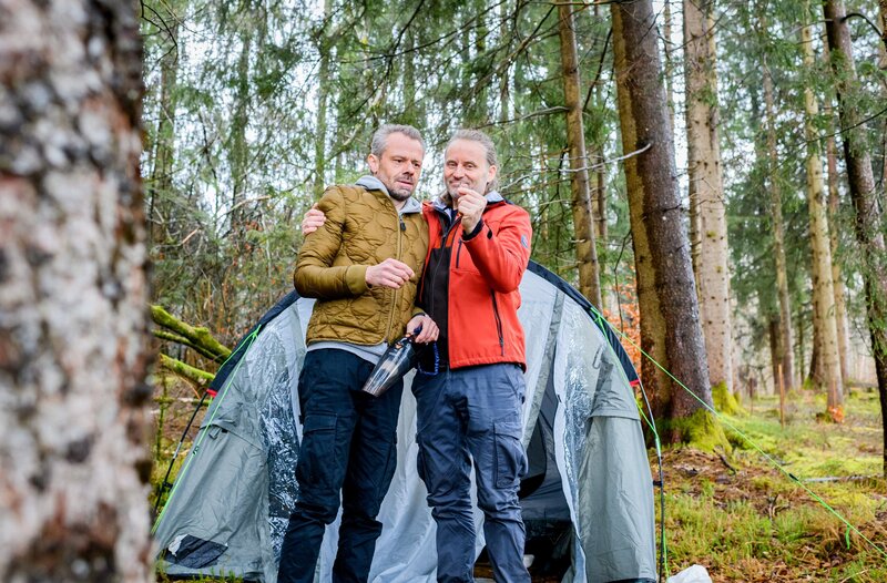 Erik (Sven Waasner, l.) und Michael (Erich Altenkopf, r.) feiern sich stolz als Überlebende einer Bärenattacke. – Bild: ORF/​ARD/​Christof Arnold