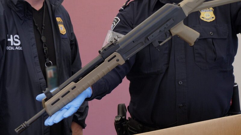 Ein CBP-Beamter hält eine Schusswaffe in der Hand, die bei einer Lieferung von Lautsprechern beschlagnahmt wurde. (National Geographic) – Bild: Lucky8TV /​ National Geographic
