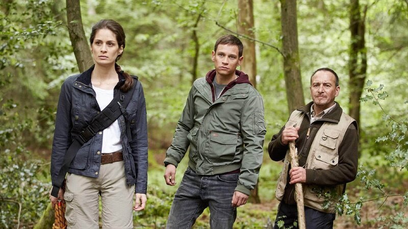 Die Forstbiologin Pia (Anna Puck) stapft mit Alex (Vinzenz Kiefer, M.) und Semir (Erdogan Atalay) durchs Unterholz zu ihrer Hütte im Wald. – Bild: TVNOW /​ Guido Engels