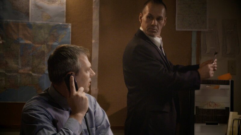 Ein Mann spricht in ein Festnetztelefon, während ein anderer Mann ihn beobachtet – Bild: Crime + Investigation /​ abacus media