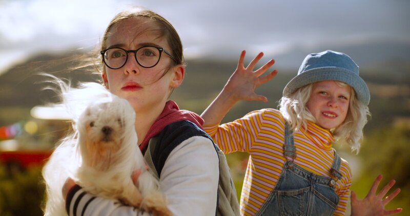 Naomi (Amy Rose Ó Hanlon) beschützt ihre Alien-Freundin Glitch (Matilda Gavin) mutig vor den bösen Wächtern, die vor einem süßen Welpen zurückschrecken. – Bild: SR/​RTÉ Irland