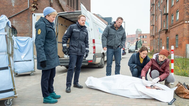 In einem Wäschetransporter taucht eine unbekannte, männliche Leiche auf. Noch am Fundort nehmen Rechtsmedizinerin Helene Sturbeck (Katharina Blaschke, r.) und die Kollegen der SOKO – Karoline Joost (Nike Fuhrmann, 2.v.r.), Lars Pöhlmann (Dominic Boeer, 3.v.l.), Timmermann (Mathias Junge, 2.v.l.) und Stine (Sidsel Hindhede, l.) den Toten in Augenschein. Offenbar ist er brutal erstochen worden. Warum musste der Mann sterben? – Bild: ZDF /​ Meyerbroeker