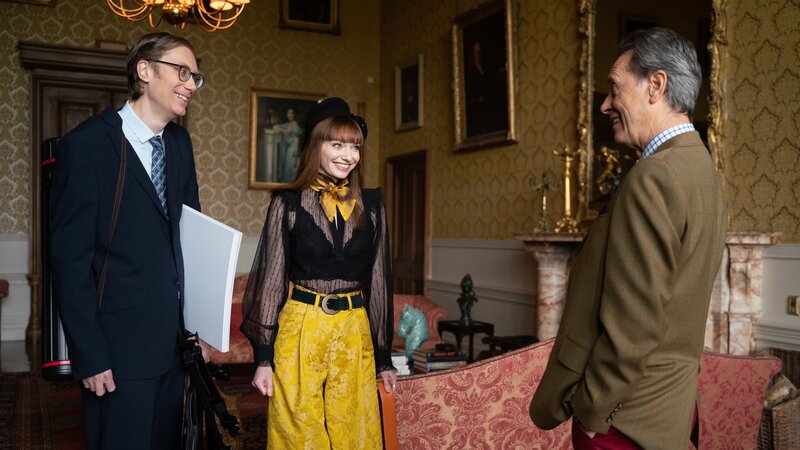 Lady Gabby (Eleanor Tomlinson, M.) ist aufgeregt. Endlich treffen sie und Greg (Stephen Merchant, l.) ihren Vater (Richard E. Grant, r.), um über ihr heißersehntes Festival zu sprechen. Was wird er zu Gabbys Herzensprojekt sagen? – Bild: ZDF und James Pardon