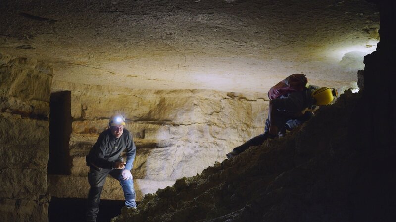 Zwei Personen erkunden unterirdische Katakomben und verwenden Speläologieausrüstung, um sich durch enge und unebene Durchgänge zu bewegen. – Bild: PERNEL MEDIA, THE HISTORY CHANNEL