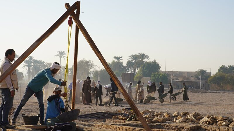 Mit Hilfe von einfachen Flaschenzügen leeren die Arbeiter die mit sandverfüllten senkrechten Schächte der Gräber. Der neuentdeckte Friedhof im sogenannten Dreieck ist eher ungewöhnlich für Theben, da die meisten Gräber dort in den Hängen des Westgebirges angelegt wurden, nicht in der Ebene. – Bild: ZDF