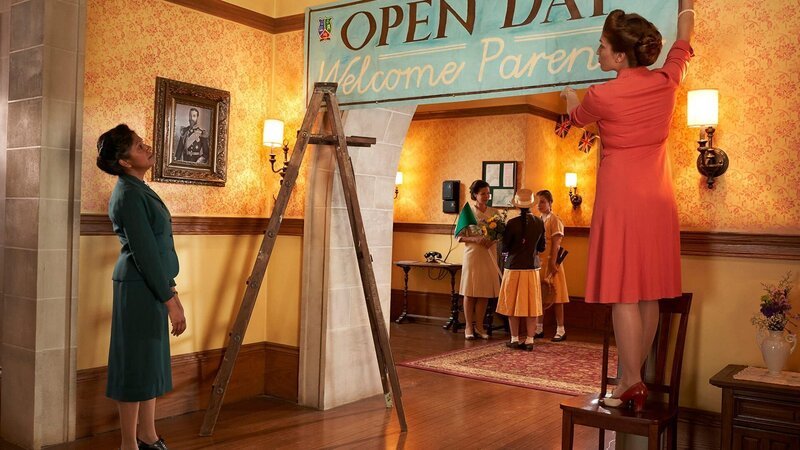 Miss Potts (Imali Perera, l.) gibt ihrer Kollegin Madame Rougier (Genevičve Beaudet, r.) Anweisungen darüber, wie sie das Begrüßungsschild an der Tür korrekt aufzuhängen hat. Es ist der Tag der offenen Tür am Internat und für die Gäste soll alles perfekt hergerichtet werden. – Bild: DHX – Malory Productions Inc./​ Queen Bert Produc