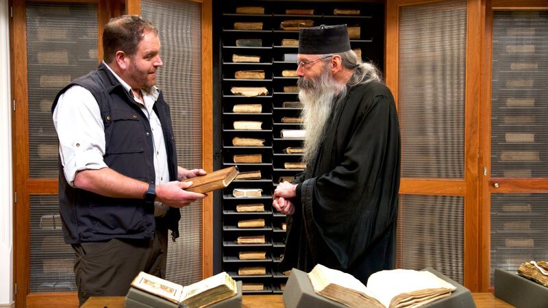 Josh Gates with Fr. Justin of Sinai in the monastery’s library in Sinai. – Bild: Warner Bros. Discovery, Inc.